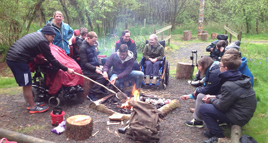 Disabled pupils of Lonsdale School sit round a fire during camping trip.