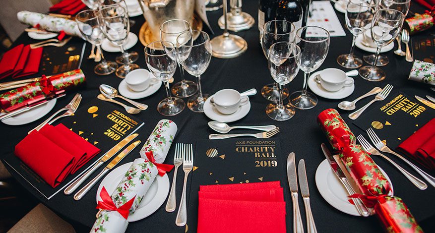 dinner table with red napkins, charity ball programme and Christmas Crackers