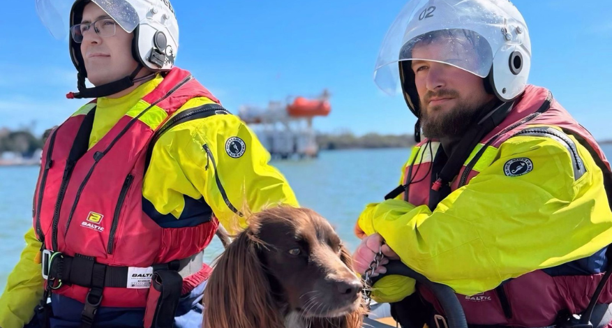 Two people in high vis and helmets with brown spaniel on lifeboat
